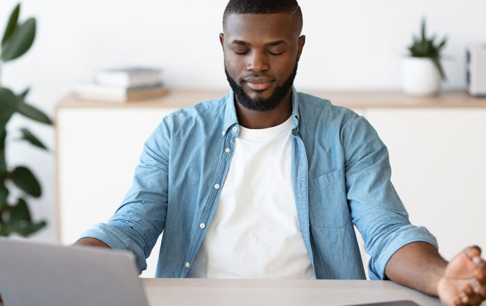 Black man with a laptop doing meditation techniques learned in therapy