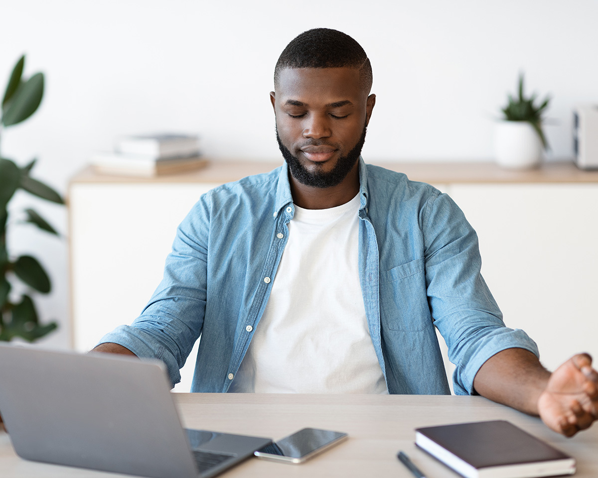 Black man with a laptop doing meditation techniques learned in therapy